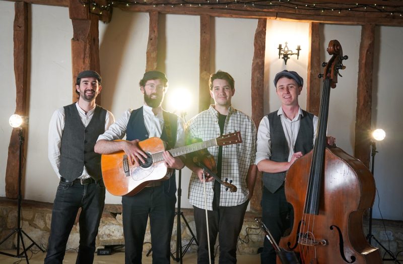 The Broadsmen standing with their instruments including the optional fiddle player